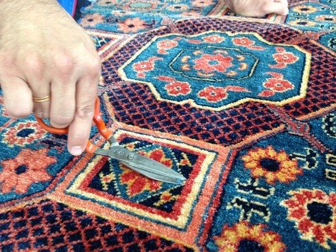 Ein Teppichmeister schneidet nach der Wäsche überstehende Fasern eines blauen Orientteppichs von Hand